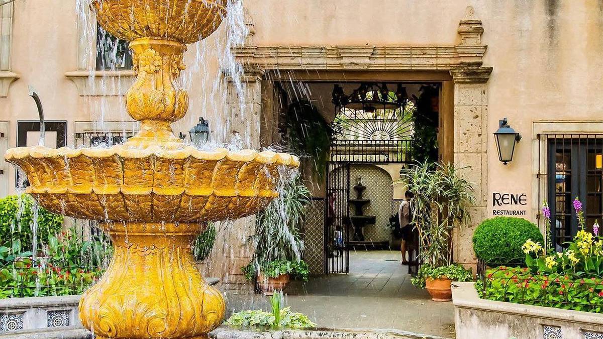 Close up photo of a running fountain on the left with the entrance and sigh for Rene's in the background on a sunny day in Sedona, Arizona, USA
